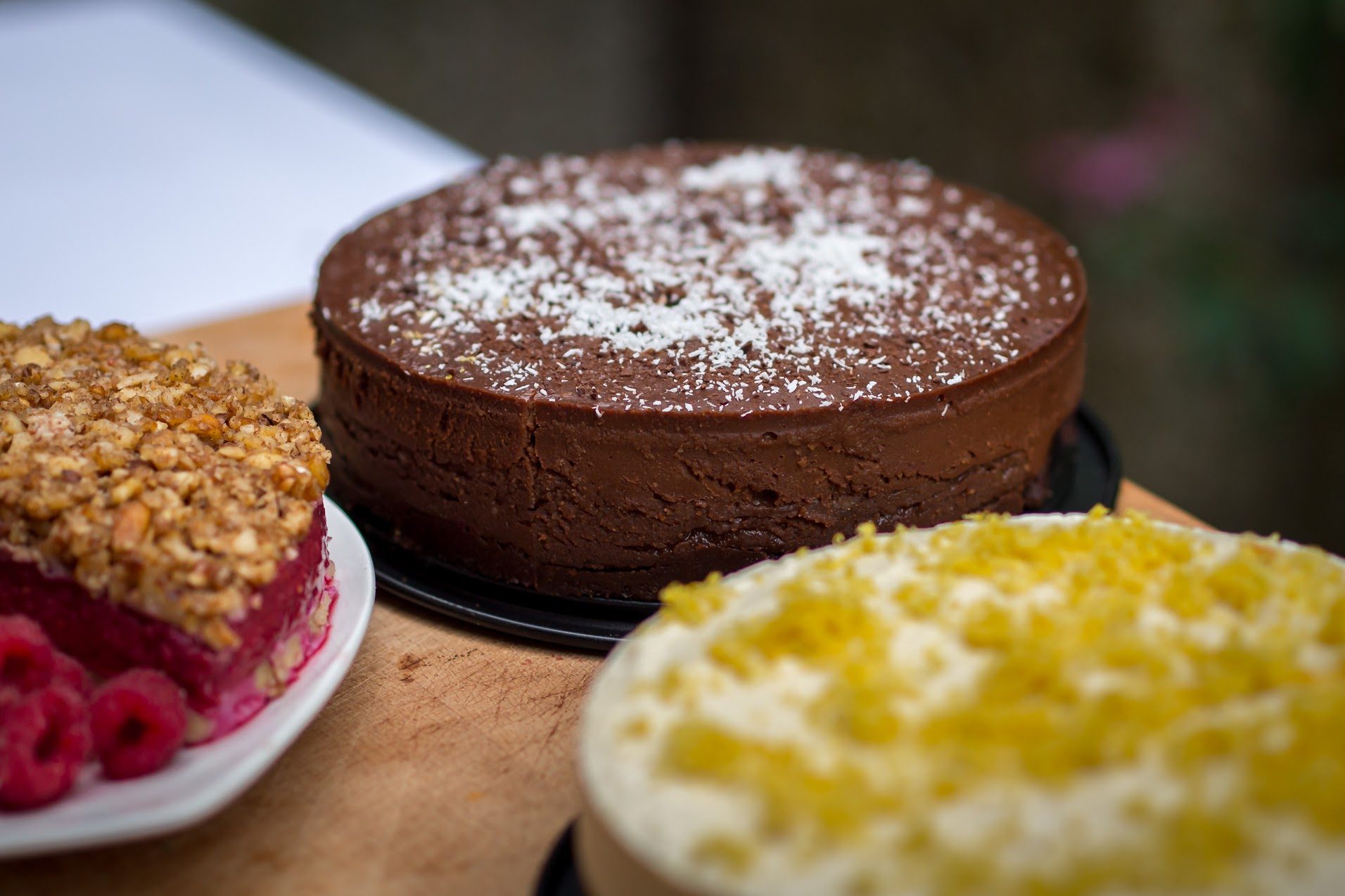Rosy Raspberry Crumble, Chocoholics Dream Cake and Cheeky Lemon Cheesecake on a wooden table