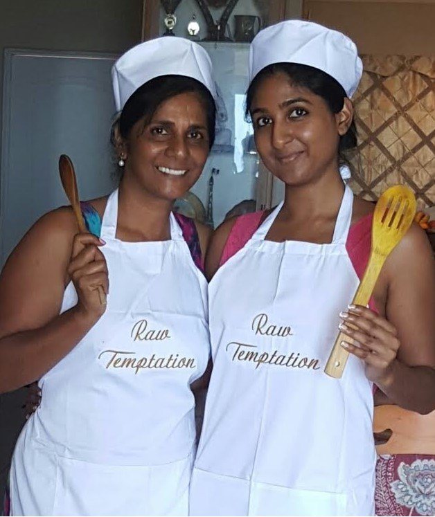 Sharon and Candice Chetty in Raw Temptation aprons and chef's hats, holding wooden spoons