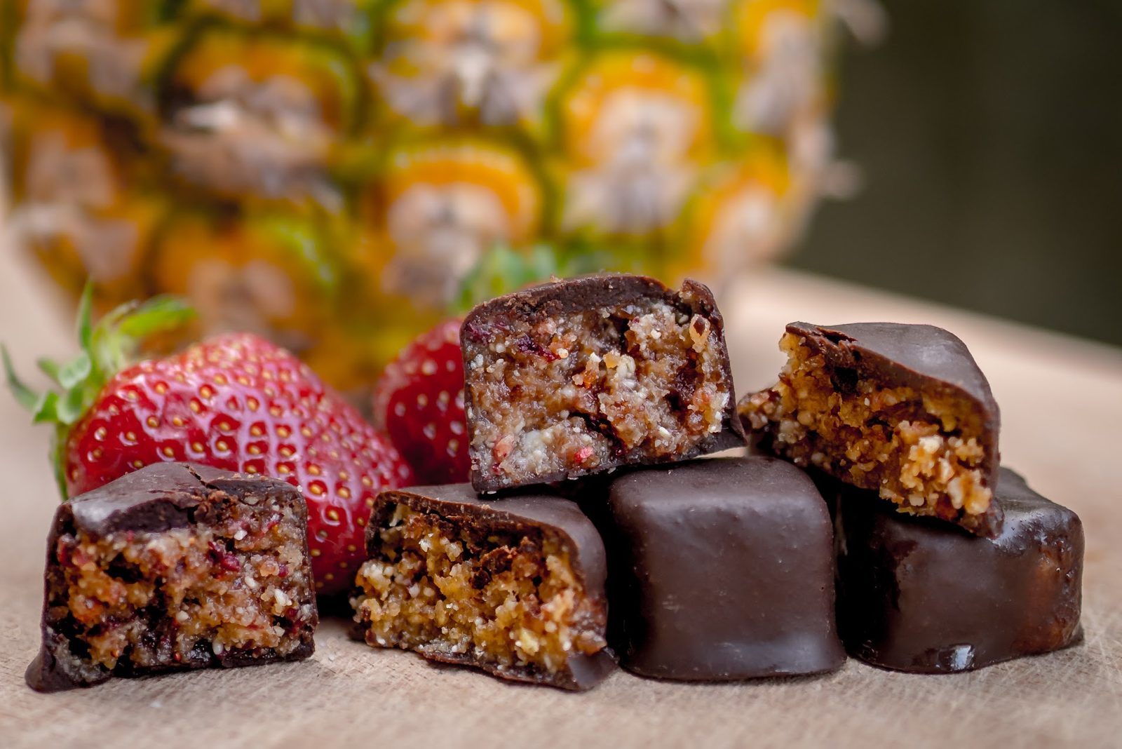 A pineapple praline cut open to show its raw filling, with fresh strawberries and a pineapple behind