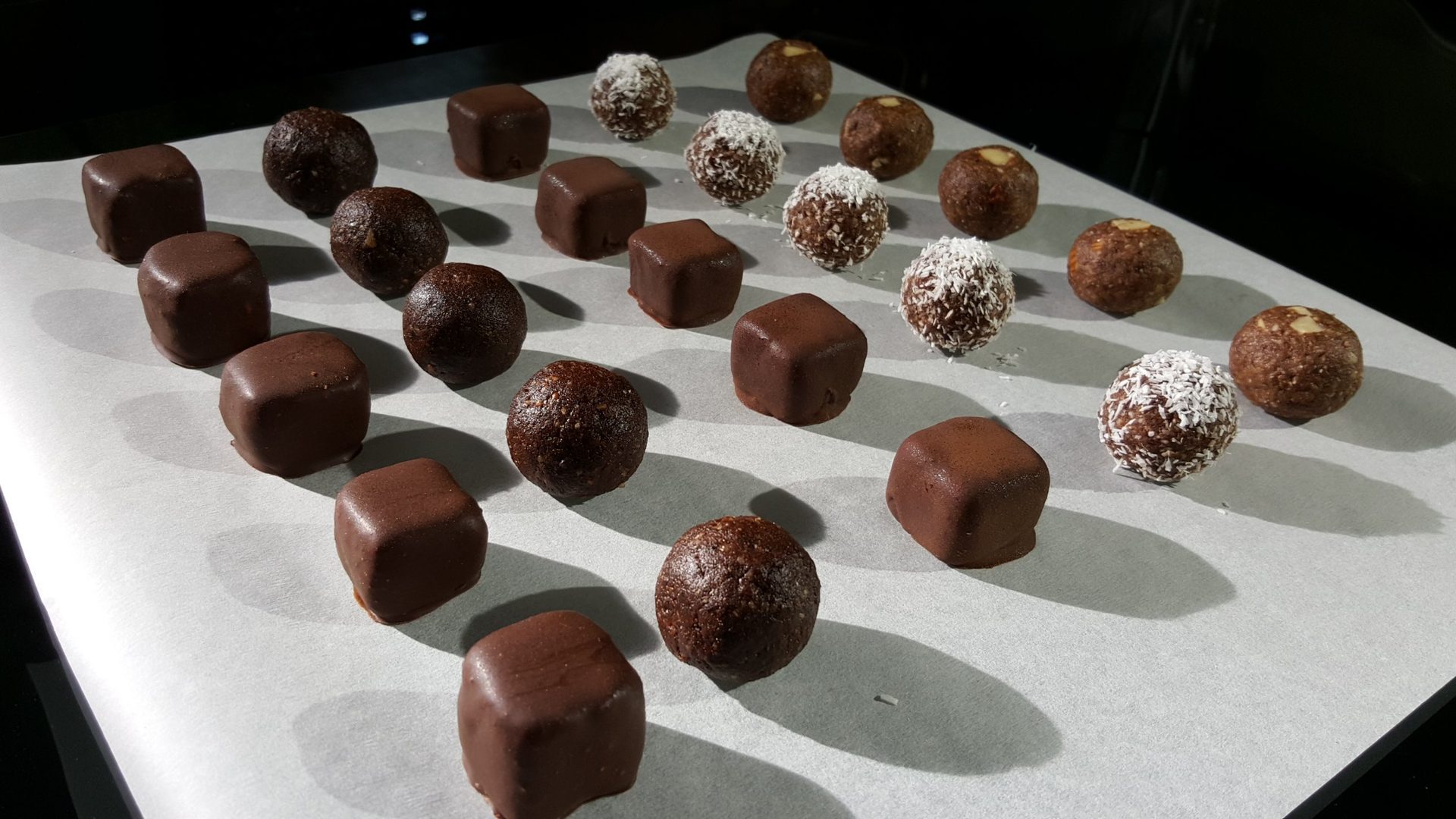 Rows of freshly enrobed pralines and coconut truffles on baking paper